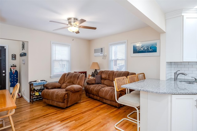 living room with ceiling fan, sink, a wall mounted AC, and light wood-type flooring