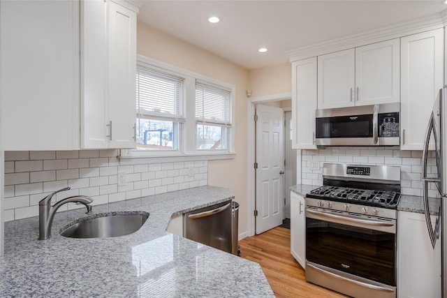 kitchen featuring white cabinets, stainless steel appliances, sink, light stone counters, and light hardwood / wood-style flooring