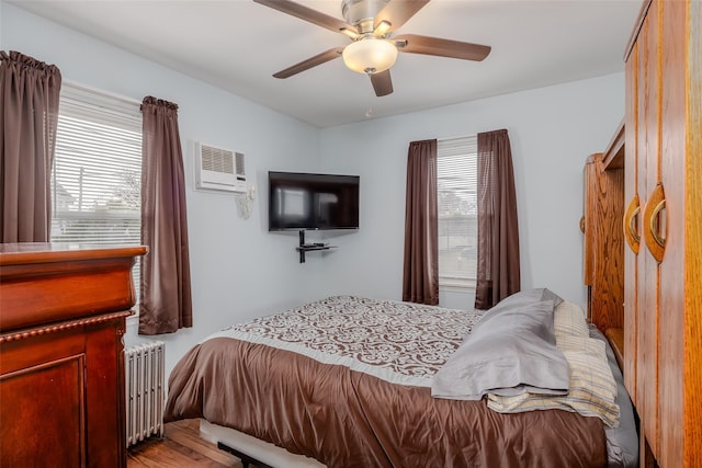 bedroom featuring ceiling fan, an AC wall unit, radiator, and light hardwood / wood-style flooring