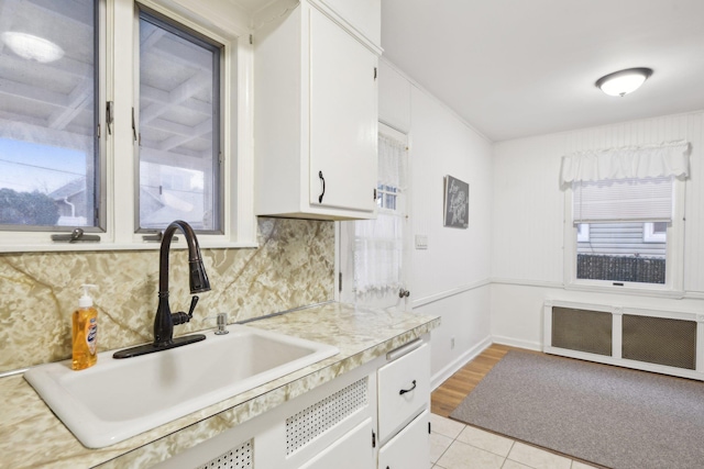 kitchen featuring sink, white cabinets, radiator, light tile patterned flooring, and decorative backsplash