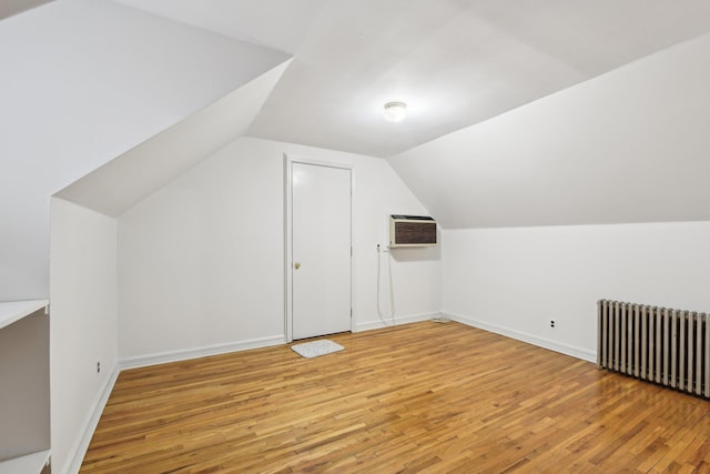 bonus room with an AC wall unit, radiator, lofted ceiling, and light hardwood / wood-style flooring