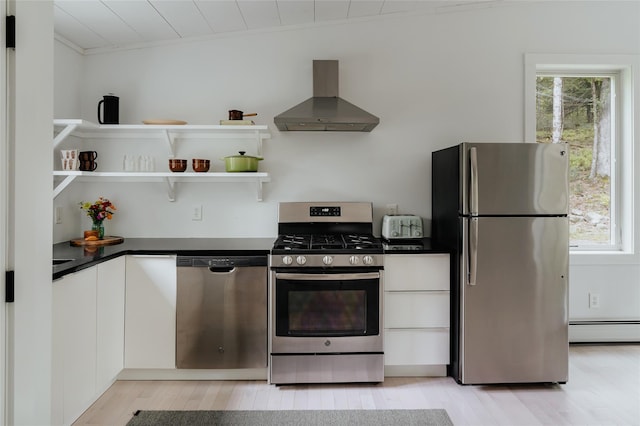 kitchen featuring white cabinetry, a baseboard heating unit, appliances with stainless steel finishes, light wood-type flooring, and wall chimney exhaust hood