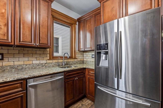 kitchen with sink, light stone counters, light wood-type flooring, appliances with stainless steel finishes, and decorative backsplash