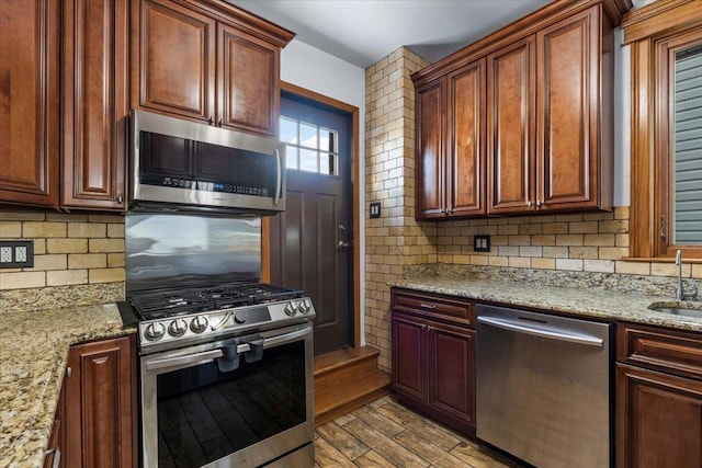 kitchen with stainless steel appliances, light stone countertops, sink, and backsplash