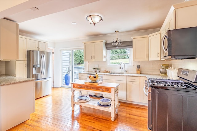 kitchen with sink, hanging light fixtures, stainless steel appliances, tasteful backsplash, and light hardwood / wood-style floors