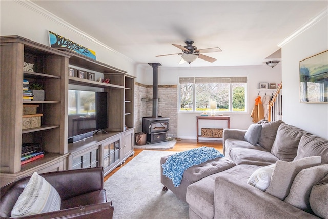 living room featuring crown molding, ceiling fan, wood-type flooring, and a wood stove