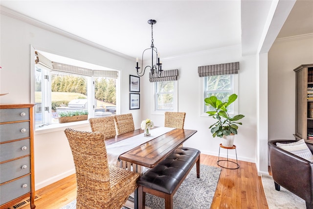 dining area with an inviting chandelier, light hardwood / wood-style flooring, and ornamental molding