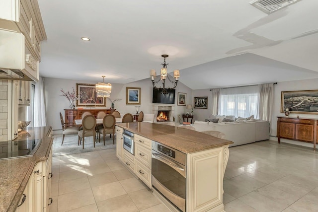 kitchen featuring cream cabinetry, hanging light fixtures, oven, vaulted ceiling, and a chandelier