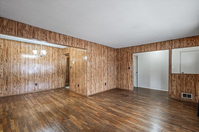 unfurnished room with dark hardwood / wood-style flooring, an inviting chandelier, and wooden walls