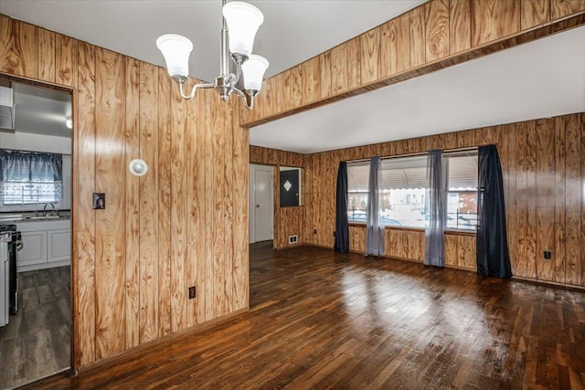 empty room featuring sink, dark hardwood / wood-style flooring, a notable chandelier, and wooden walls