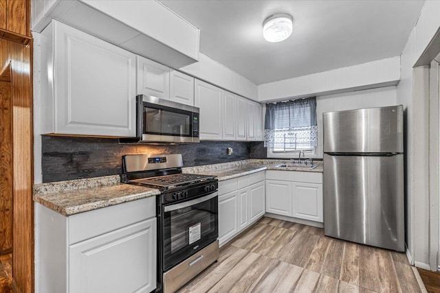 kitchen with appliances with stainless steel finishes, sink, white cabinets, backsplash, and light stone counters