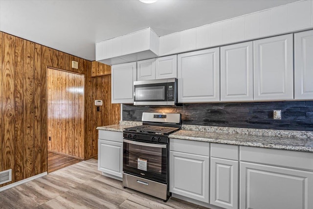 kitchen featuring white cabinetry, wood walls, appliances with stainless steel finishes, and light stone counters