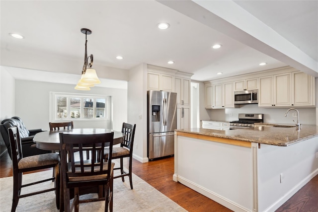 kitchen with kitchen peninsula, wood-type flooring, hanging light fixtures, appliances with stainless steel finishes, and light stone countertops