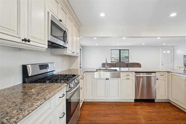 kitchen with kitchen peninsula, appliances with stainless steel finishes, dark hardwood / wood-style floors, light stone counters, and sink