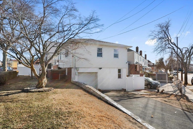 view of side of property with driveway, an attached garage, fence, a yard, and stucco siding