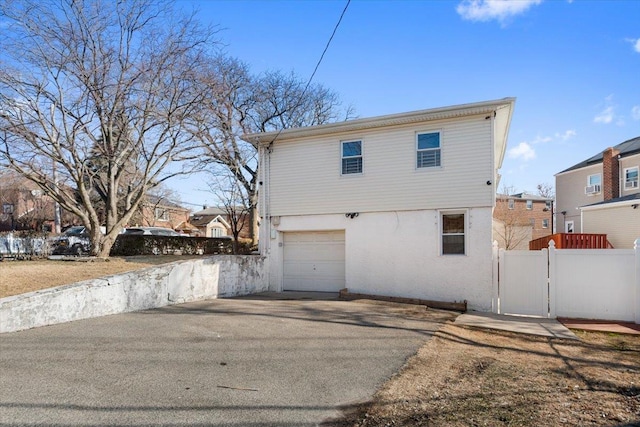 exterior space featuring driveway, a residential view, an attached garage, fence, and stucco siding