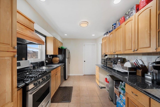 kitchen featuring light tile patterned floors, stainless steel appliances, tasteful backsplash, a sink, and dark stone counters