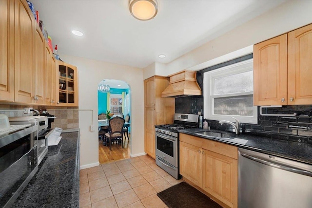 kitchen with arched walkways, custom range hood, glass insert cabinets, stainless steel appliances, and a sink