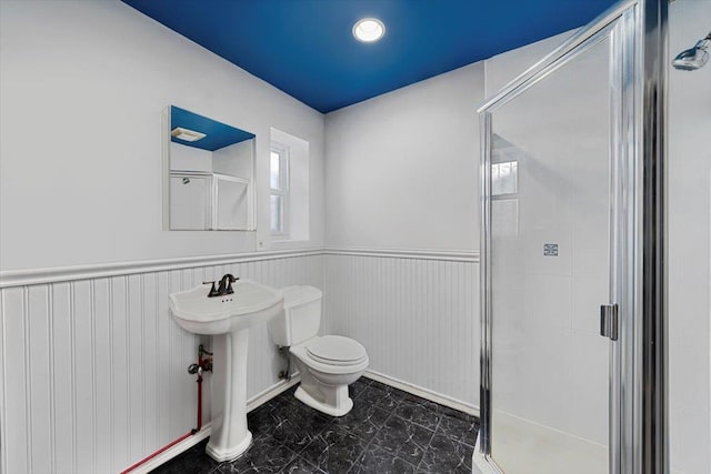 bathroom with a wainscoted wall, a stall shower, a sink, and toilet