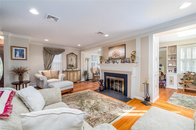 living room featuring light wood-type flooring, baseboard heating, ornamental molding, and built in features