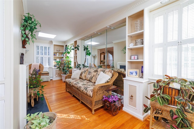 living room featuring built in shelves, wood-type flooring, a skylight, and crown molding