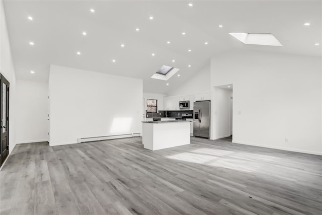 unfurnished living room with baseboard heating, light hardwood / wood-style flooring, high vaulted ceiling, and a skylight