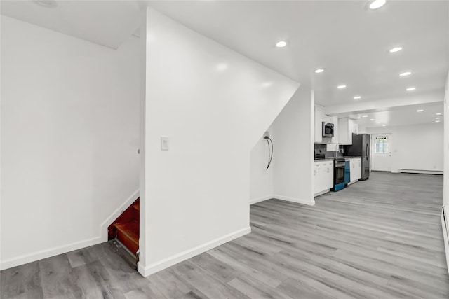 interior space with light hardwood / wood-style floors, a baseboard radiator, white cabinets, and appliances with stainless steel finishes