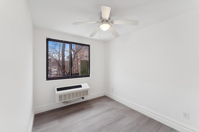 spare room with ceiling fan, an AC wall unit, heating unit, and light wood-type flooring