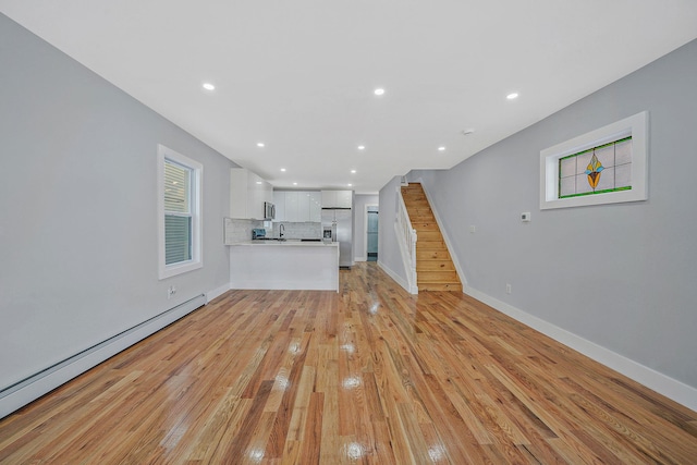 unfurnished living room featuring a baseboard heating unit, sink, and light hardwood / wood-style floors