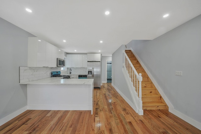 kitchen with tasteful backsplash, kitchen peninsula, light wood-type flooring, appliances with stainless steel finishes, and white cabinets