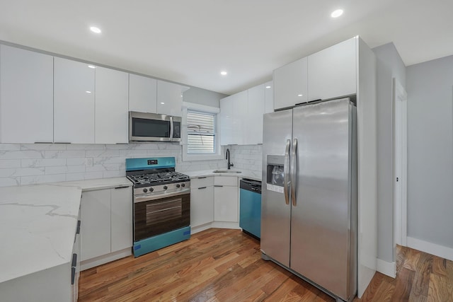 kitchen with white cabinetry, hardwood / wood-style floors, stainless steel appliances, light stone counters, and sink