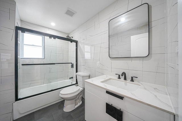 full bathroom featuring tile patterned flooring, vanity, bath / shower combo with glass door, toilet, and tile walls