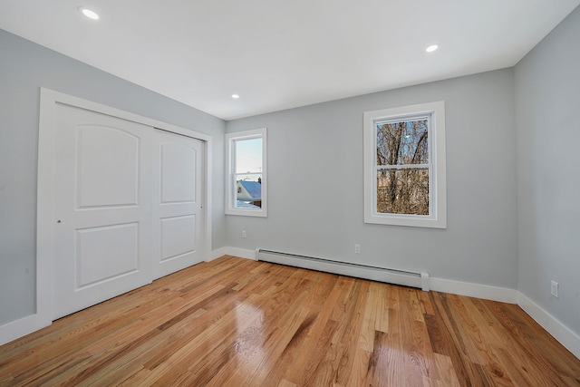 unfurnished bedroom with a baseboard heating unit, a closet, light hardwood / wood-style flooring, and multiple windows