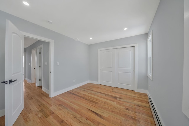 unfurnished bedroom featuring light wood-type flooring, a closet, and a baseboard heating unit