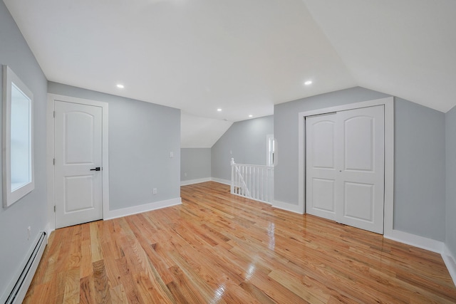 additional living space featuring a baseboard radiator, light hardwood / wood-style flooring, and vaulted ceiling