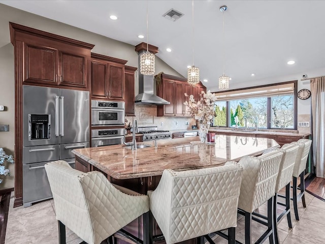 kitchen with light stone countertops, a spacious island, pendant lighting, appliances with stainless steel finishes, and a kitchen bar