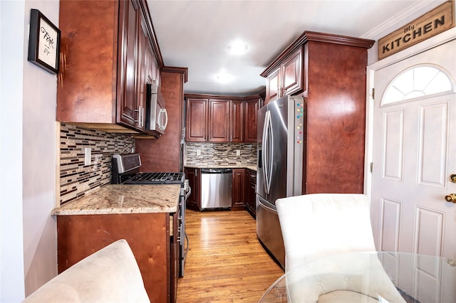 kitchen with backsplash, light hardwood / wood-style floors, light stone countertops, appliances with stainless steel finishes, and ornamental molding