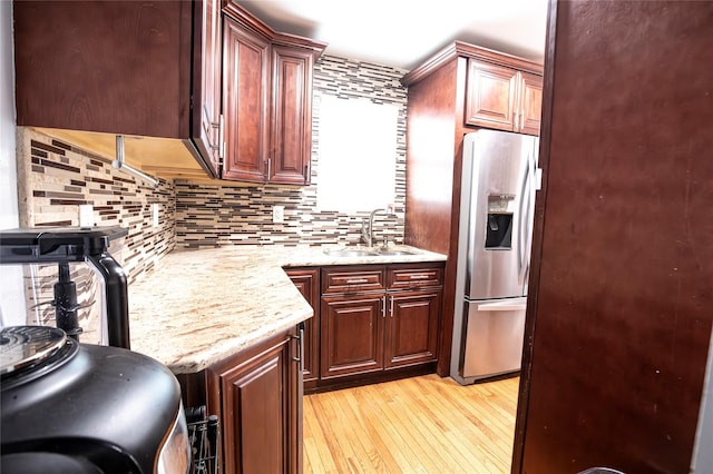 kitchen with light stone countertops, stainless steel refrigerator with ice dispenser, decorative backsplash, sink, and light wood-type flooring