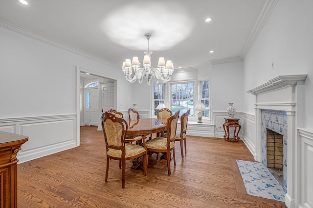 dining area with ornamental molding, light hardwood / wood-style floors, a tile fireplace, and a notable chandelier