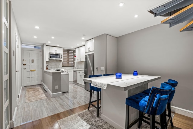 kitchen featuring tasteful backsplash, light hardwood / wood-style flooring, appliances with stainless steel finishes, a breakfast bar area, and white cabinets