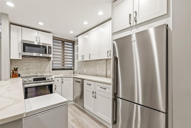 kitchen featuring appliances with stainless steel finishes, tasteful backsplash, white cabinets, light stone counters, and sink