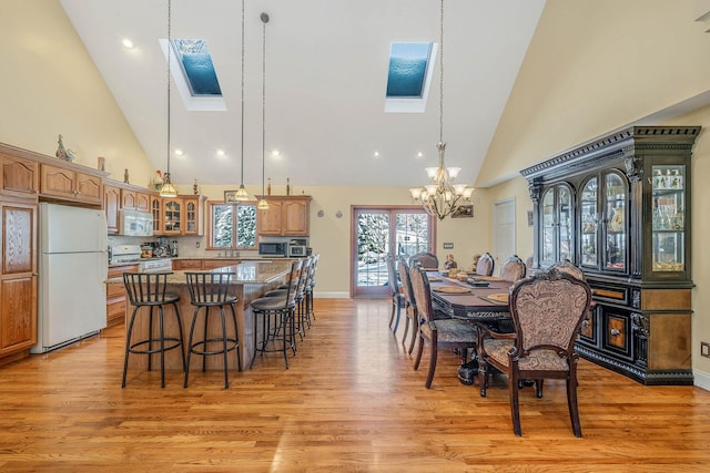 dining room featuring high vaulted ceiling, light hardwood / wood-style flooring, and a skylight