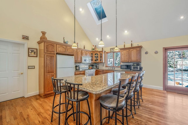 kitchen with sink, light stone countertops, white appliances, a skylight, and a kitchen island