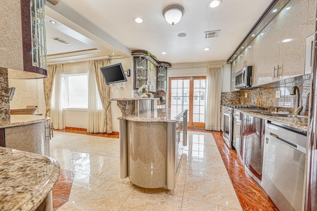 kitchen featuring sink, stainless steel appliances, light stone countertops, decorative backsplash, and a raised ceiling