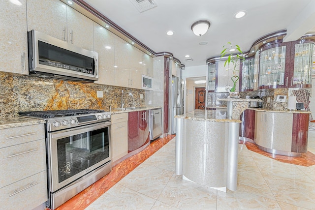 kitchen with appliances with stainless steel finishes, sink, light stone counters, and decorative backsplash