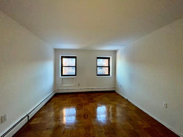 empty room with dark parquet flooring and a baseboard heating unit