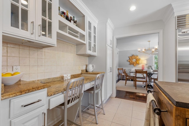 kitchen with light tile patterned floors, white cabinets, built in study area, crown molding, and backsplash