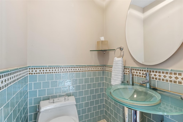 half bath featuring toilet, a sink, tile walls, and wainscoting