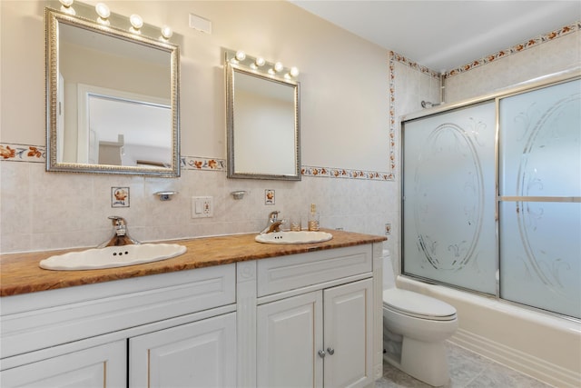 bathroom with tile patterned flooring, toilet, vanity, tile walls, and combined bath / shower with glass door