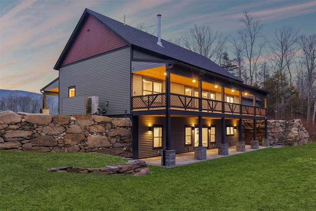 back house at dusk featuring a yard, a balcony, and a patio